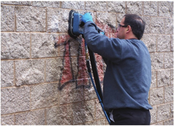 A maintenance technician uses proprietary cleaning and containment equipment to remove a tag from a split-faced black wall protected with a two-component urethane/acrylic clearcoat. Photo courtesy af Surtec Inc.